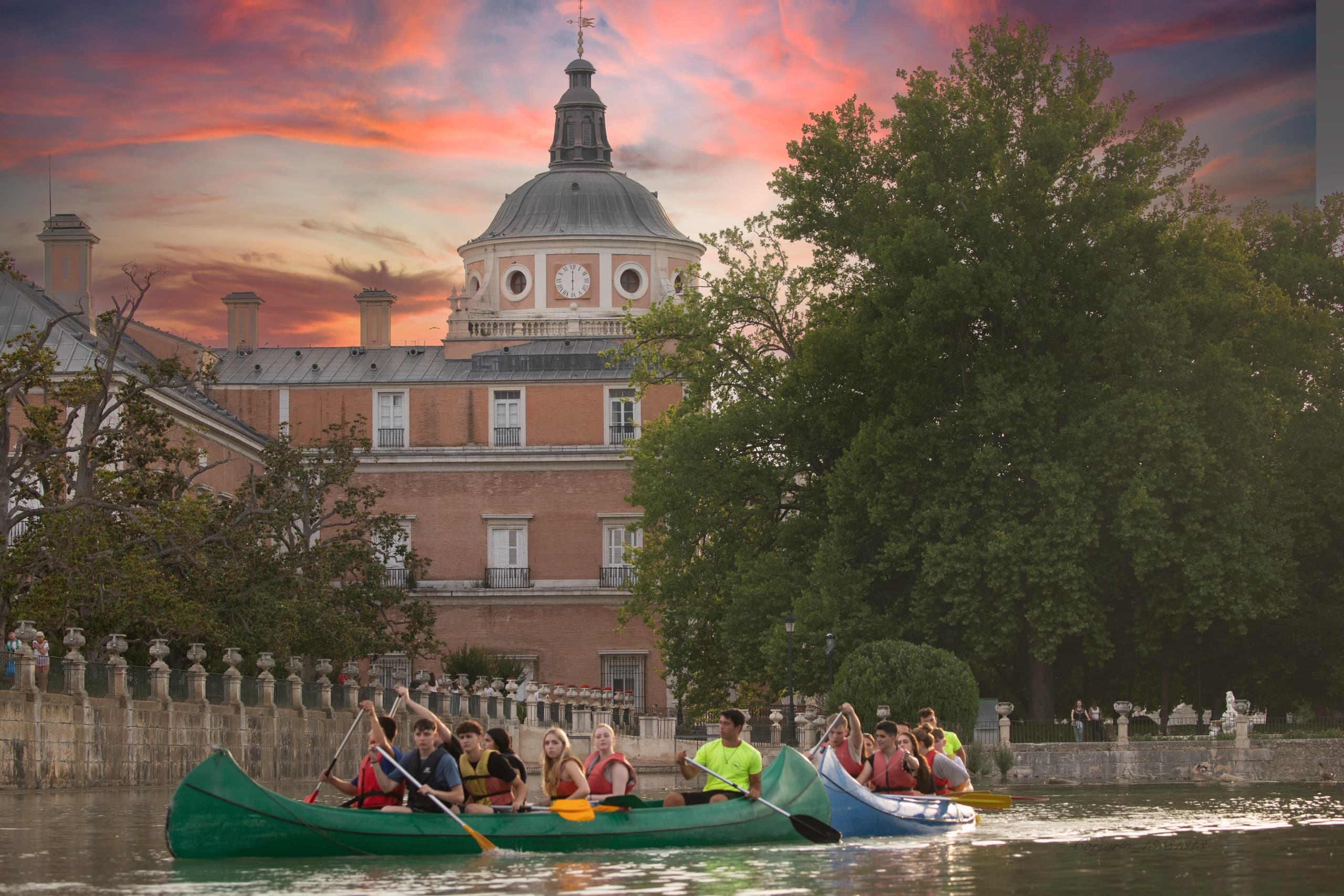 Group canoeing on river near historic Aranjuez palace at sunset