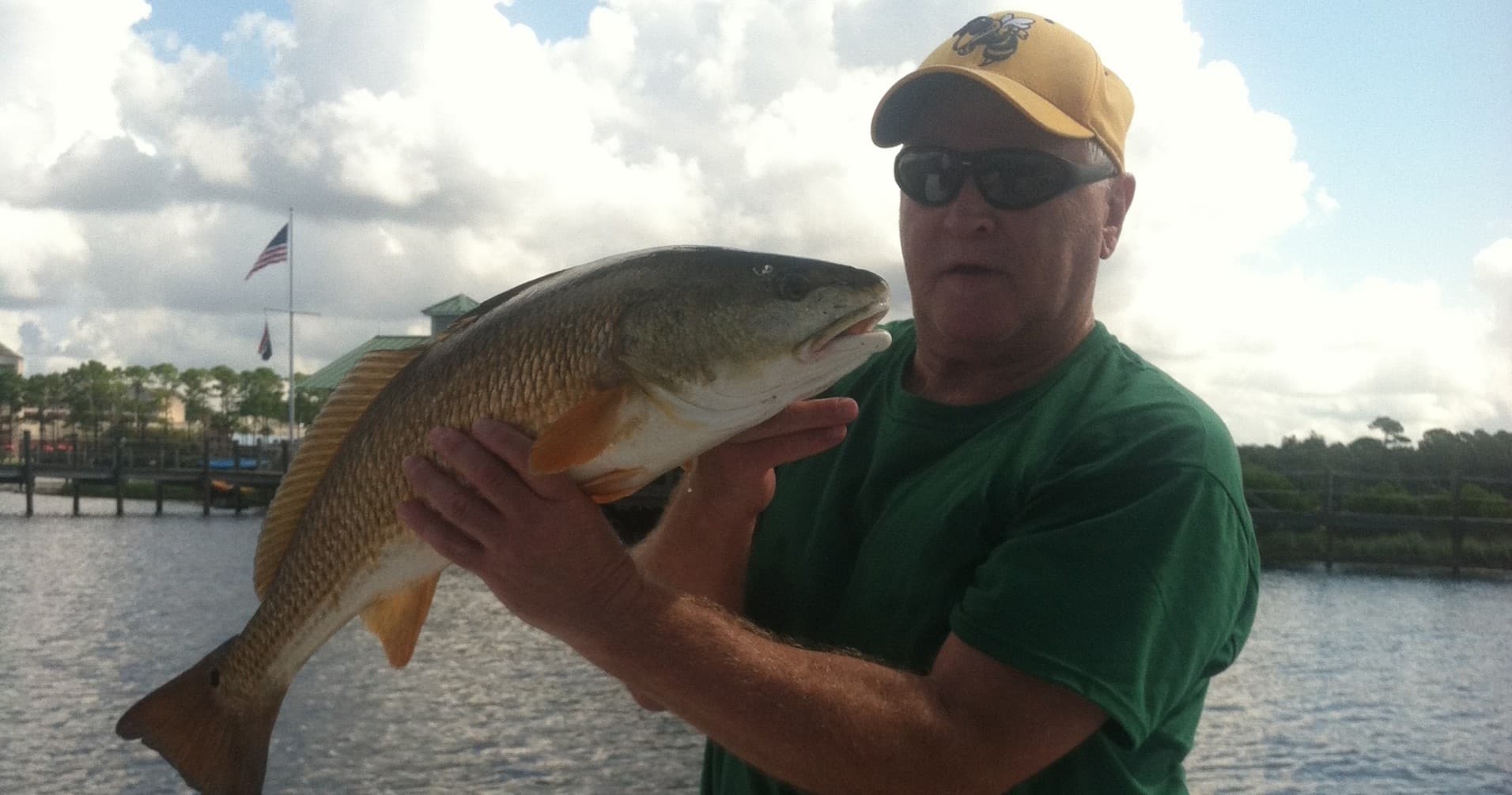 Fisherman holding big redfish near shoreline with cloudy sky