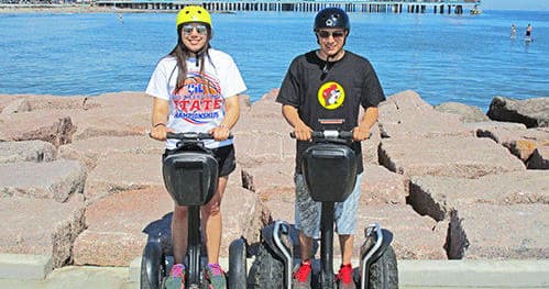 Two riders on Segways by rocky shoreline with ocean view