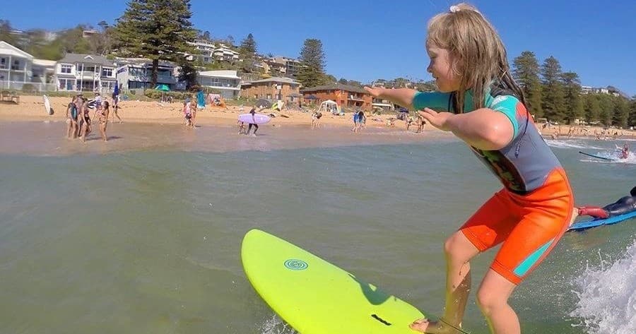 Child learning to surf on sunny Central Coast beach shore