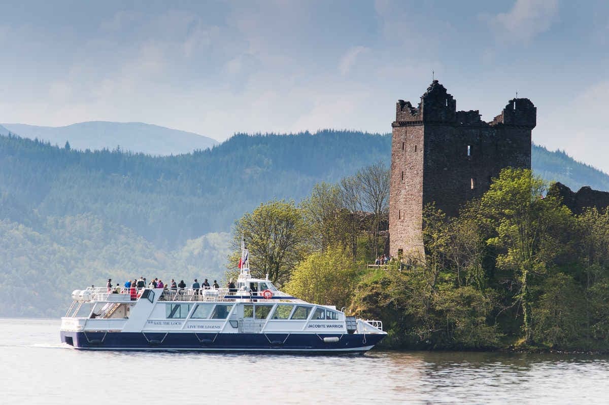 Cruise boat passing Urquhart Castle on scenic Loch Ness