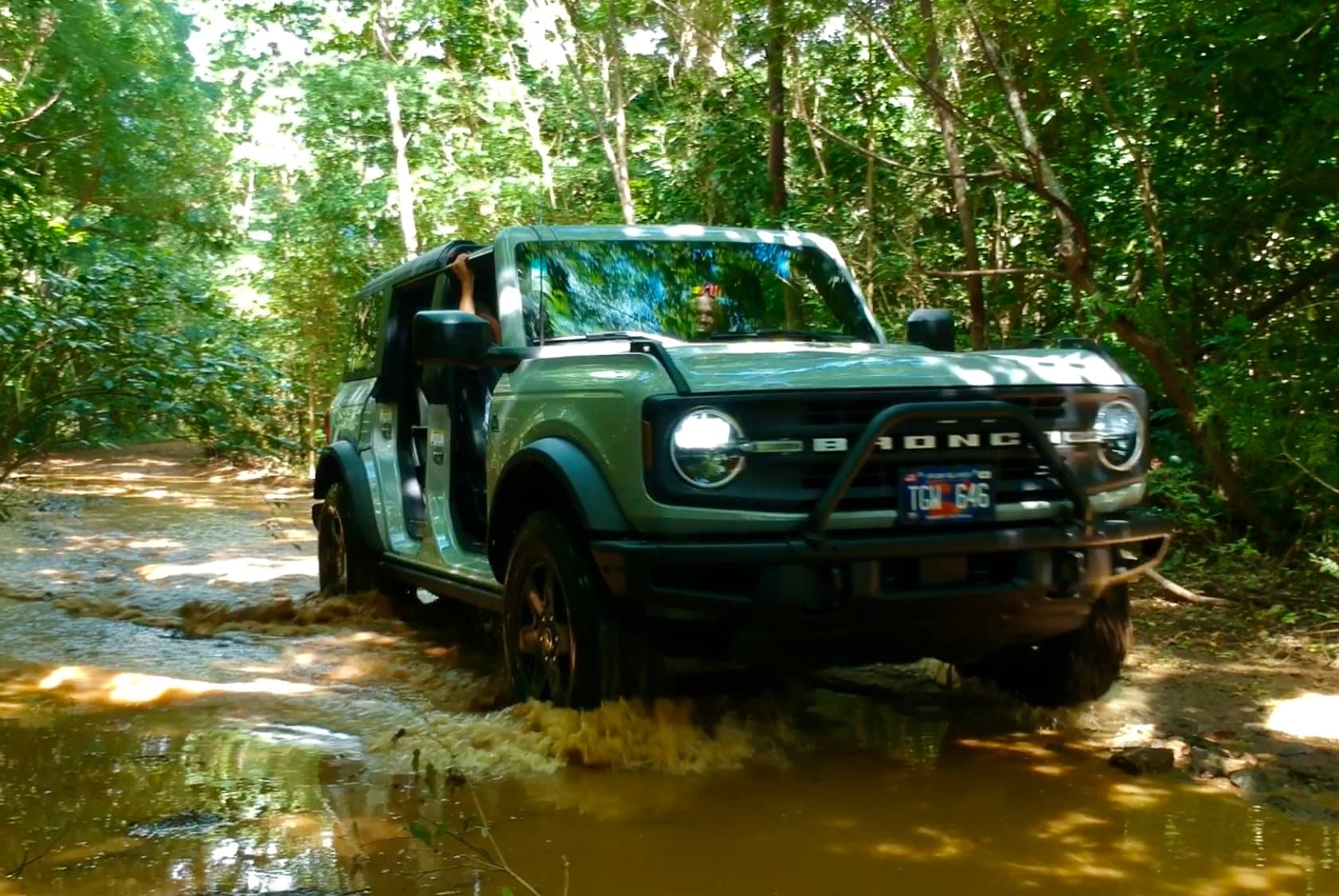 Off-road Ford Bronco splashing through forest mud trail adventure