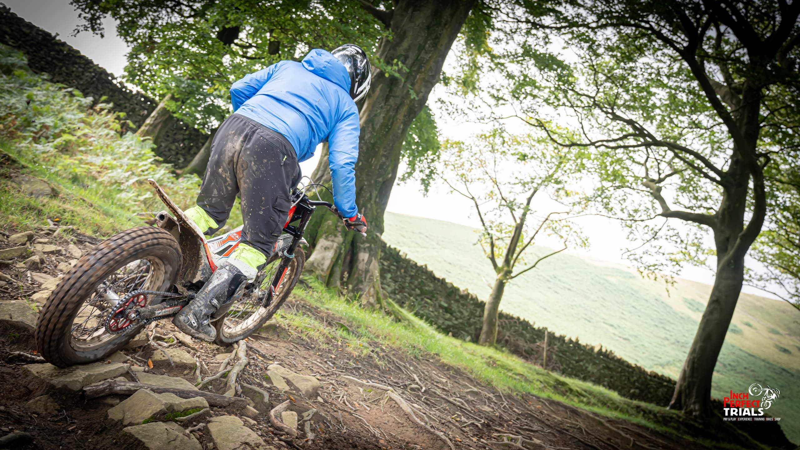 Trials rider negotiating rocky trail under tree canopy