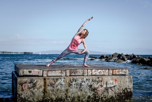 Oceanfront yoga stretch on concrete pier block by rocky shore