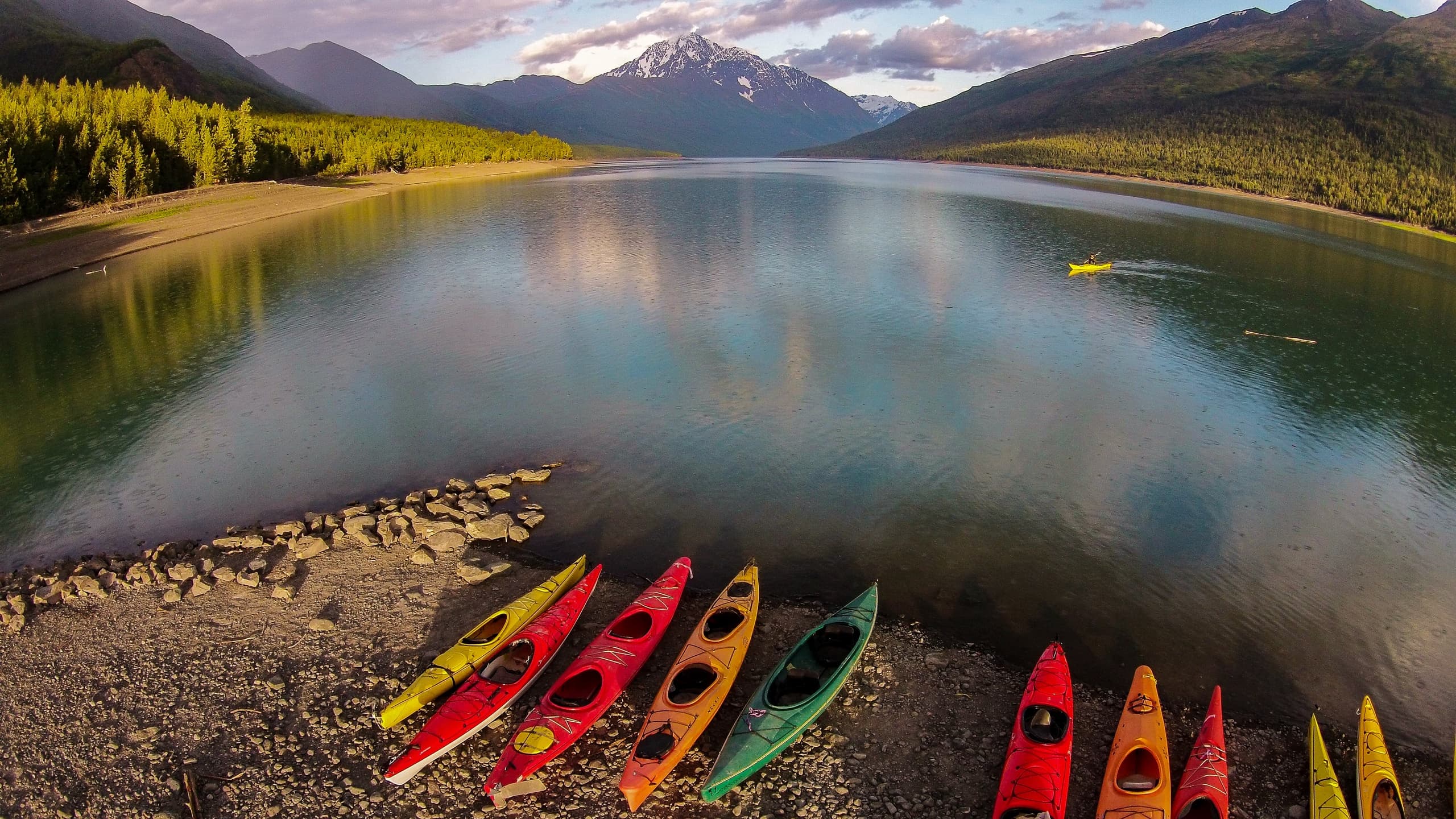 Colorful kayaks lined on lakeshore under mountain sunrise panorama