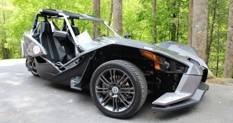 Three-wheeled roadster parked on forested country road