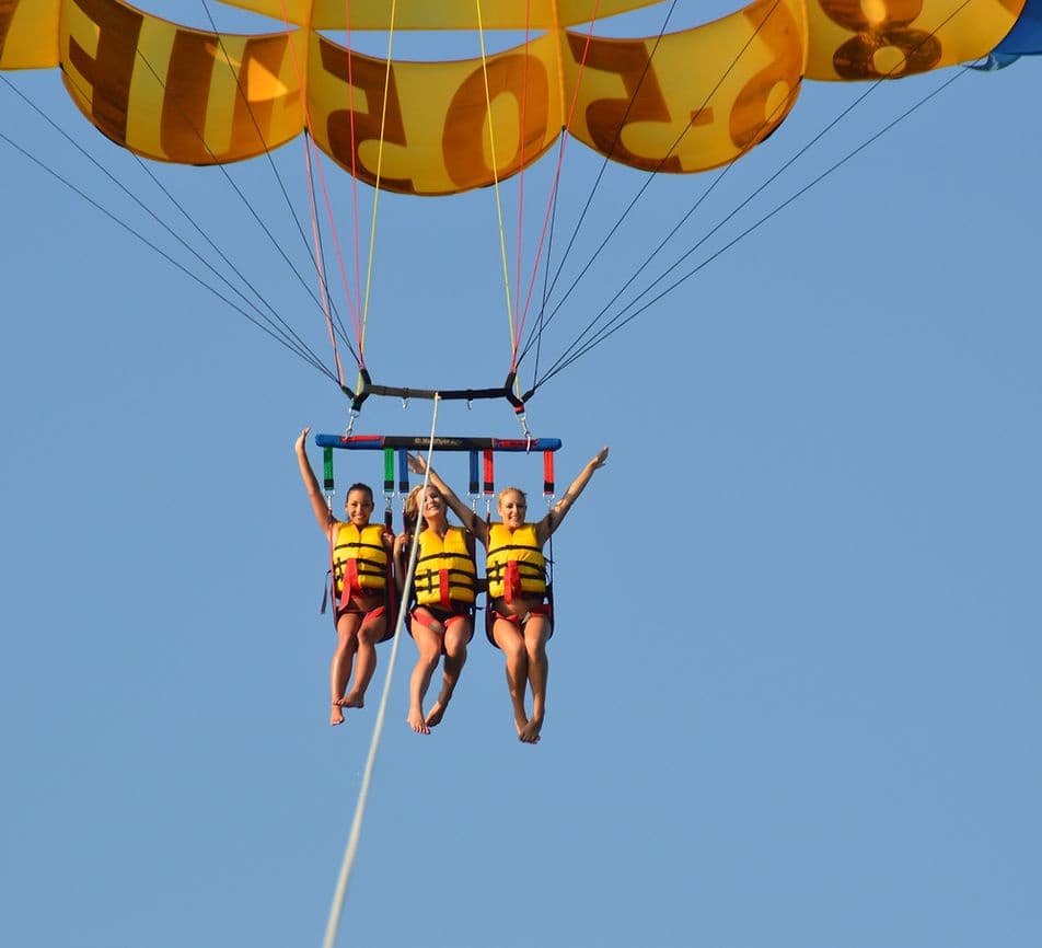 Three people parasailing under yellow canopy over bright blue ocean
