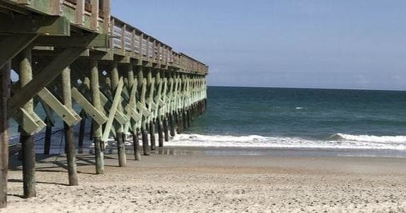 Wooden pier stretching over empty sandy beach, ocean scenery