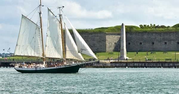 Classic tall sailboat cruising past historic fort along coastline