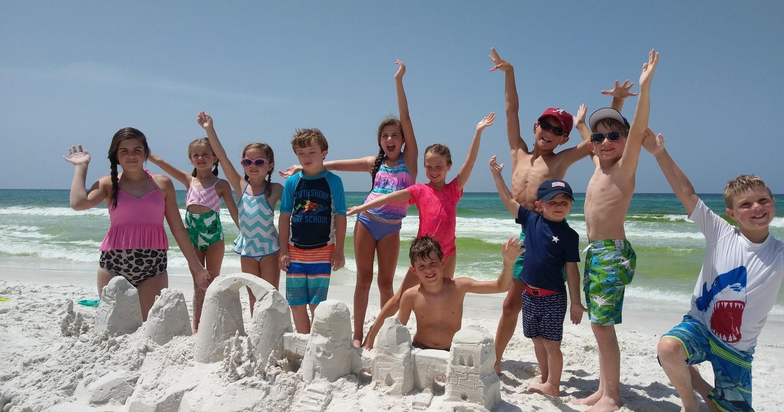 Children celebrating by sandcastle on white sandy beach