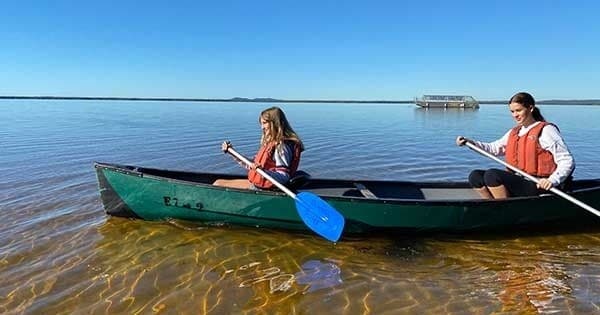 Two canoeists paddling in shallow clear water on a sunlit lake