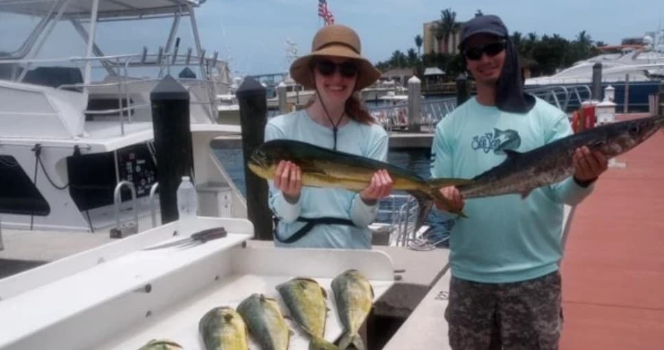 Anglers holding mahi and wahoo near marina dock after fishing trip