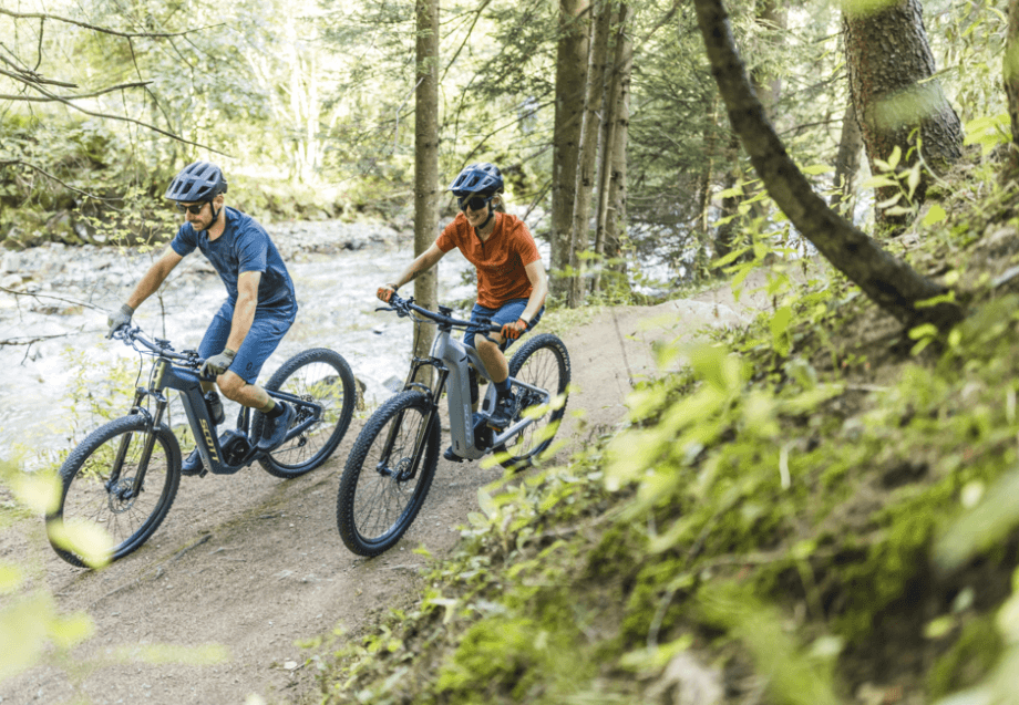 Mountain bikers riding a forest trail beside a shallow river
