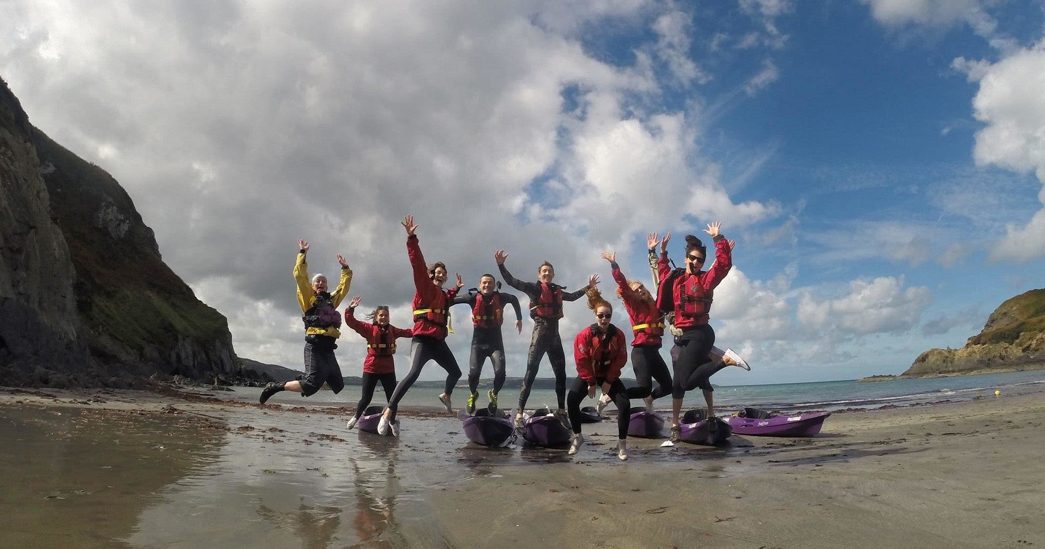 Group jumping on sandy beach after sea kayaking adventure