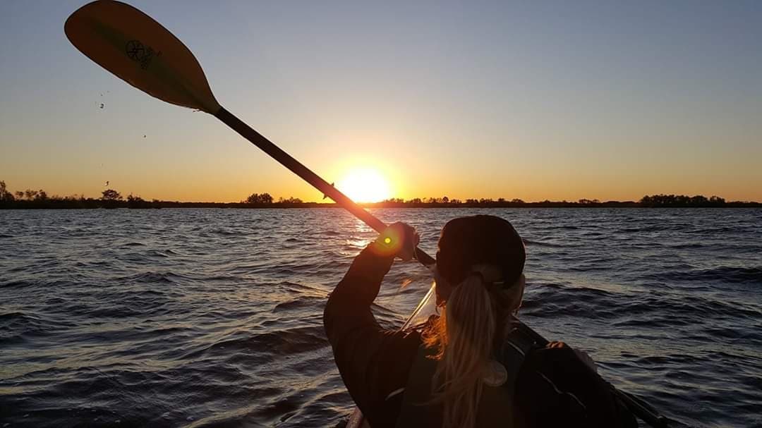 Kayaker paddling toward sunset on open water in Louisiana