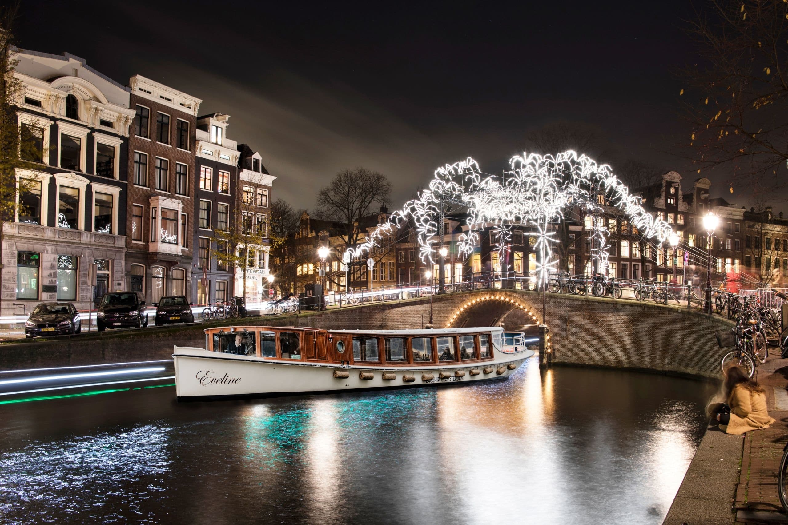 Illuminated Amsterdam canal at night with tour boat cruising