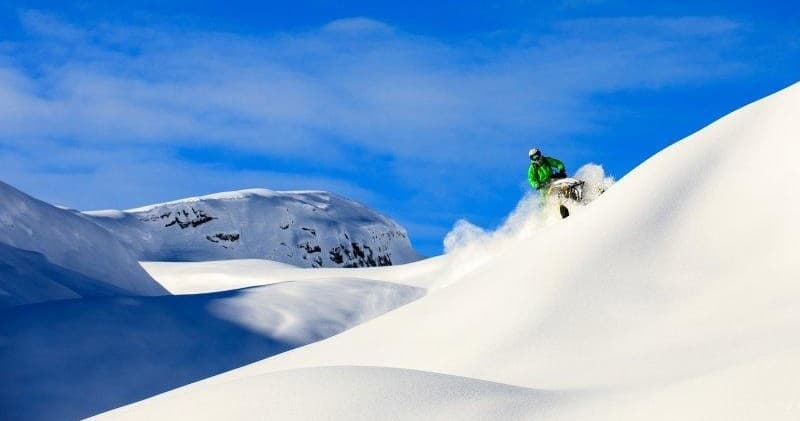 Snowmobiler carving powder across blue alpine dunes, mountain backcountry