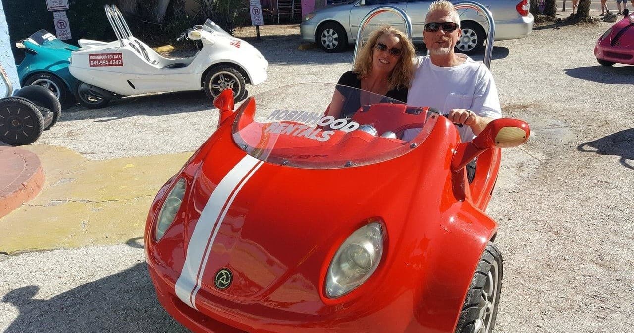 Couple driving red compact rental car on sunny beachside lot