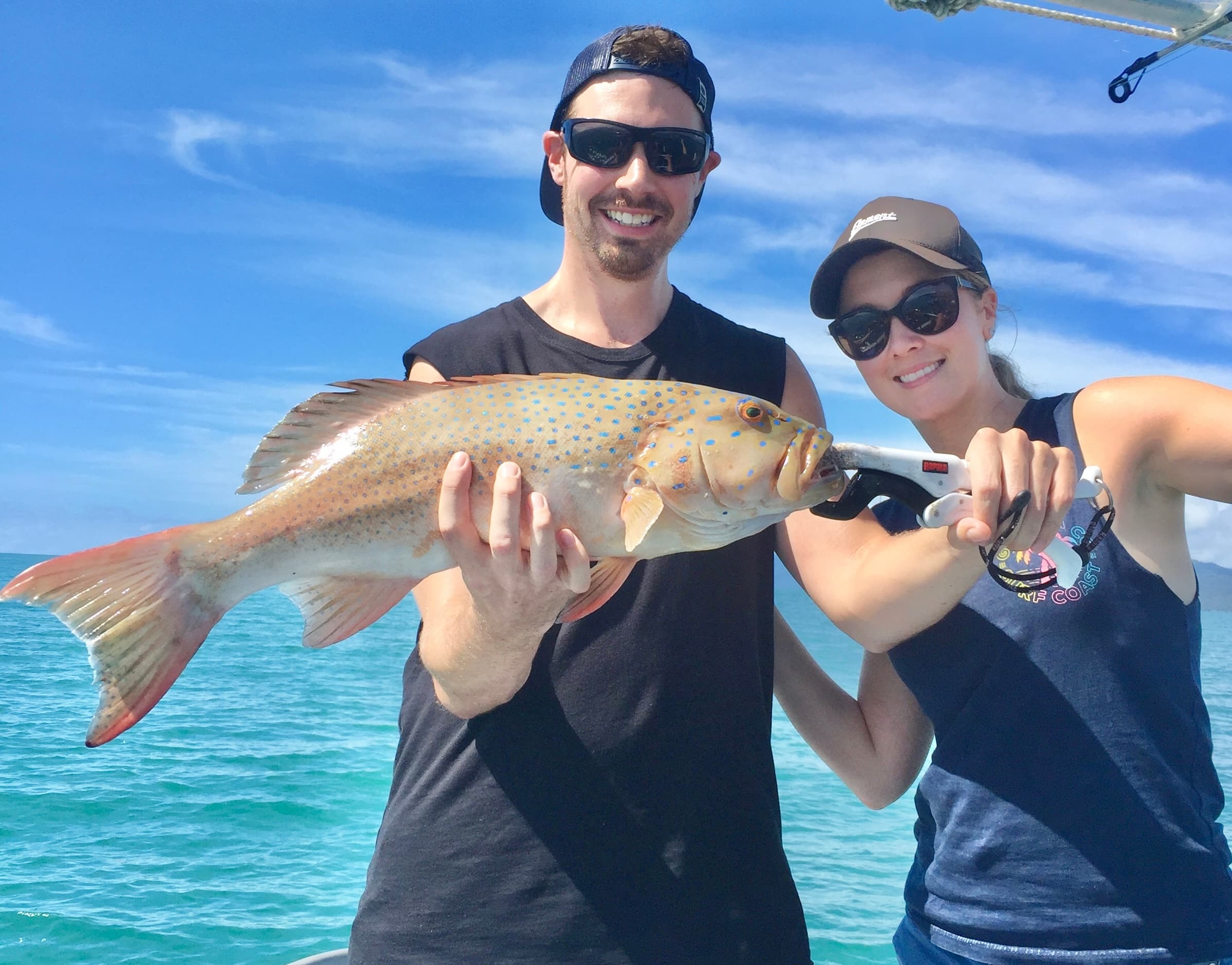 Couple holding reef fish on turquoise ocean near tropical waters