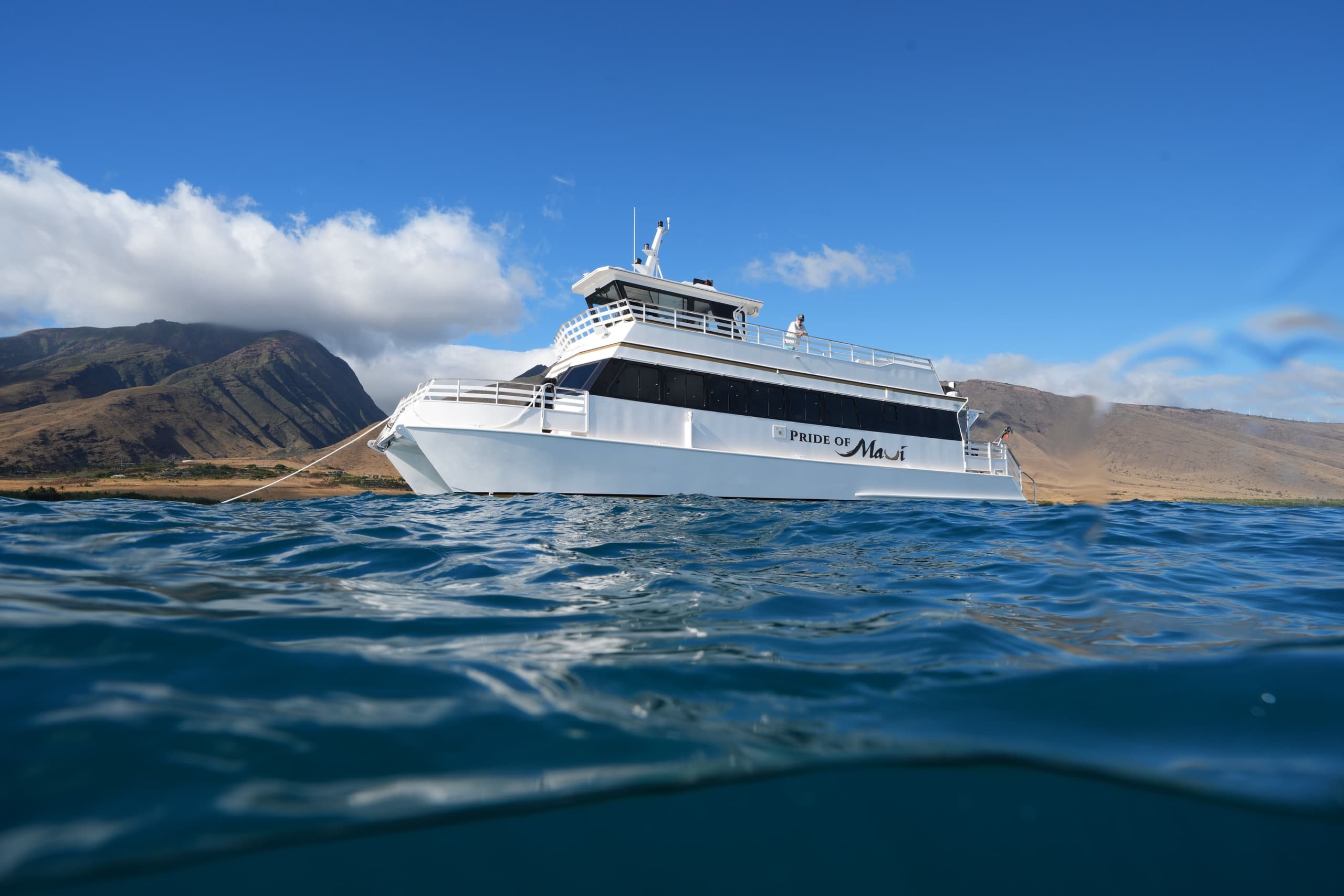 Tour catamaran cutting through ocean waves near volcanic shore