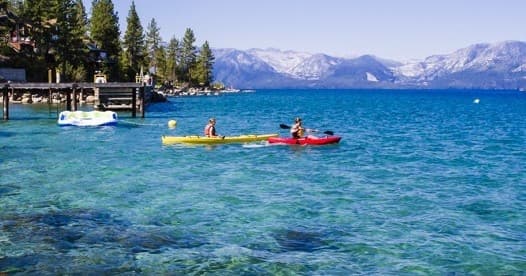 Two kayaks paddling on scenic mountain lake under sunlight