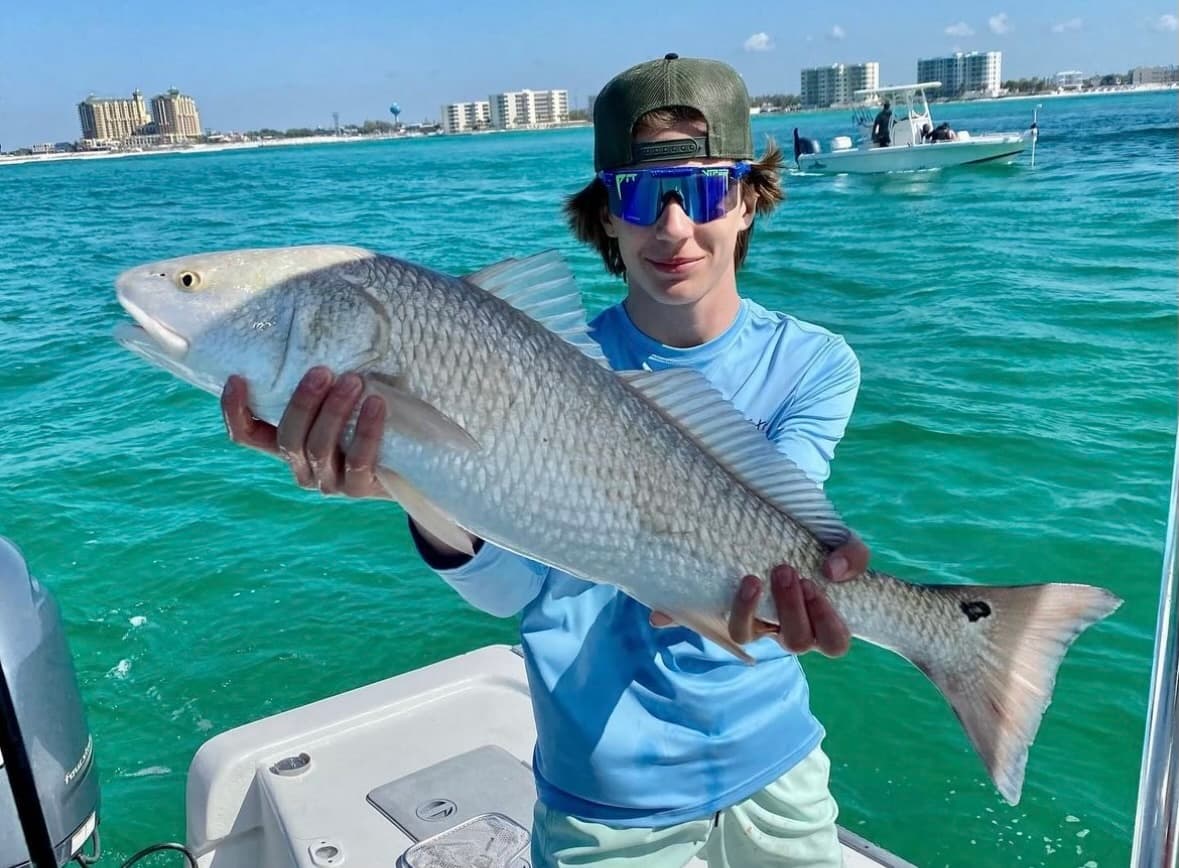 Angler holding large redfish on boat in turquoise coastal waters