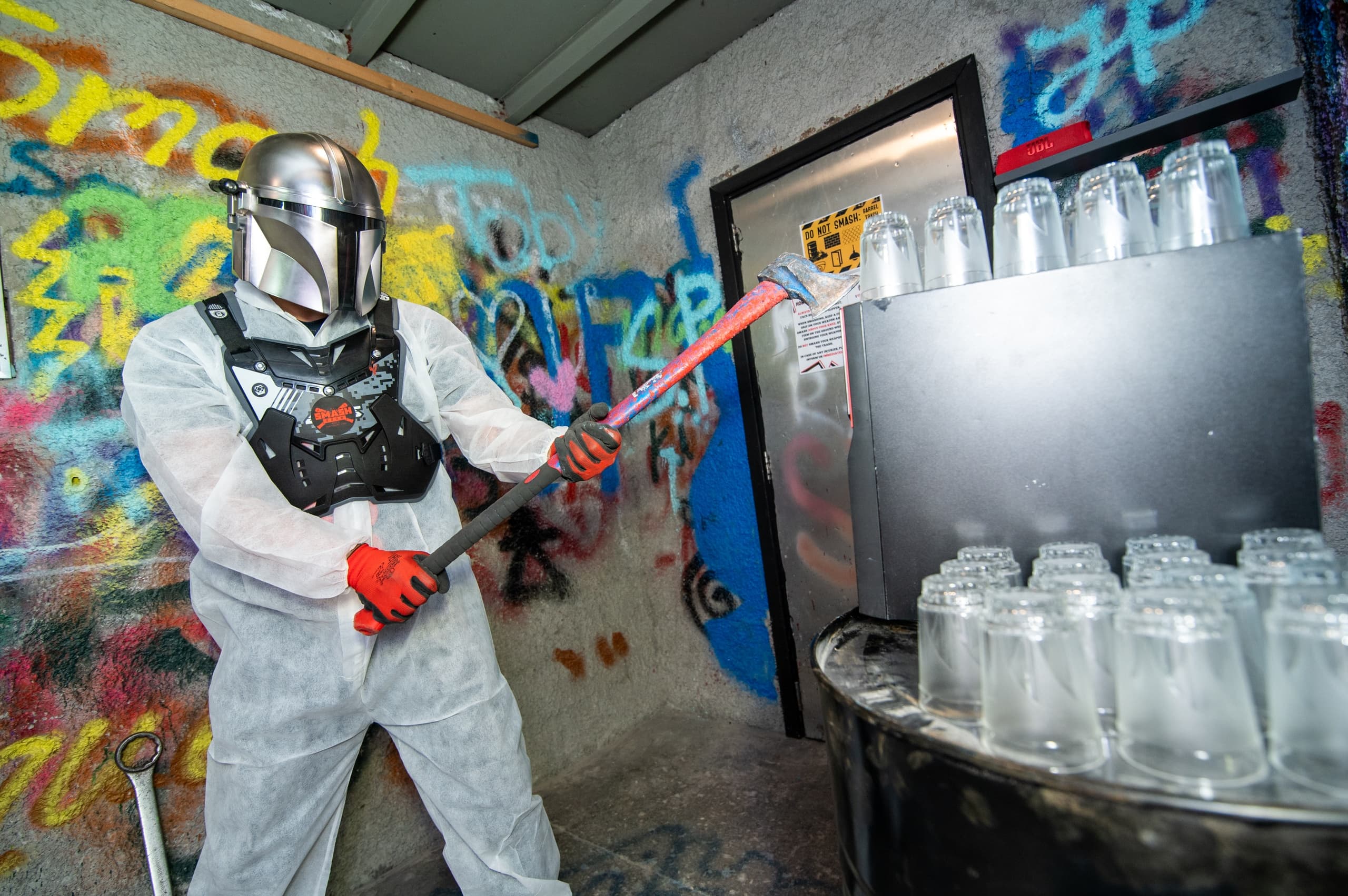 Masked participant breaking glass jars in graffiti smash room