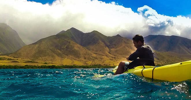 Solo kayaker observing volcanic coastline and mountains in Maui