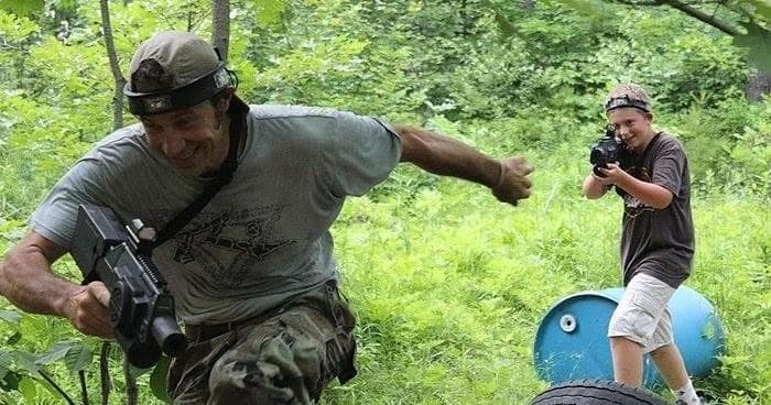 Adults playing paintball in wooded field, mid-action charge