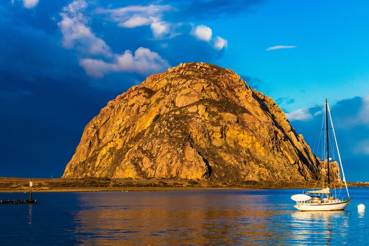 Sailboat by dramatic coastal rock at sunset, ocean adventure