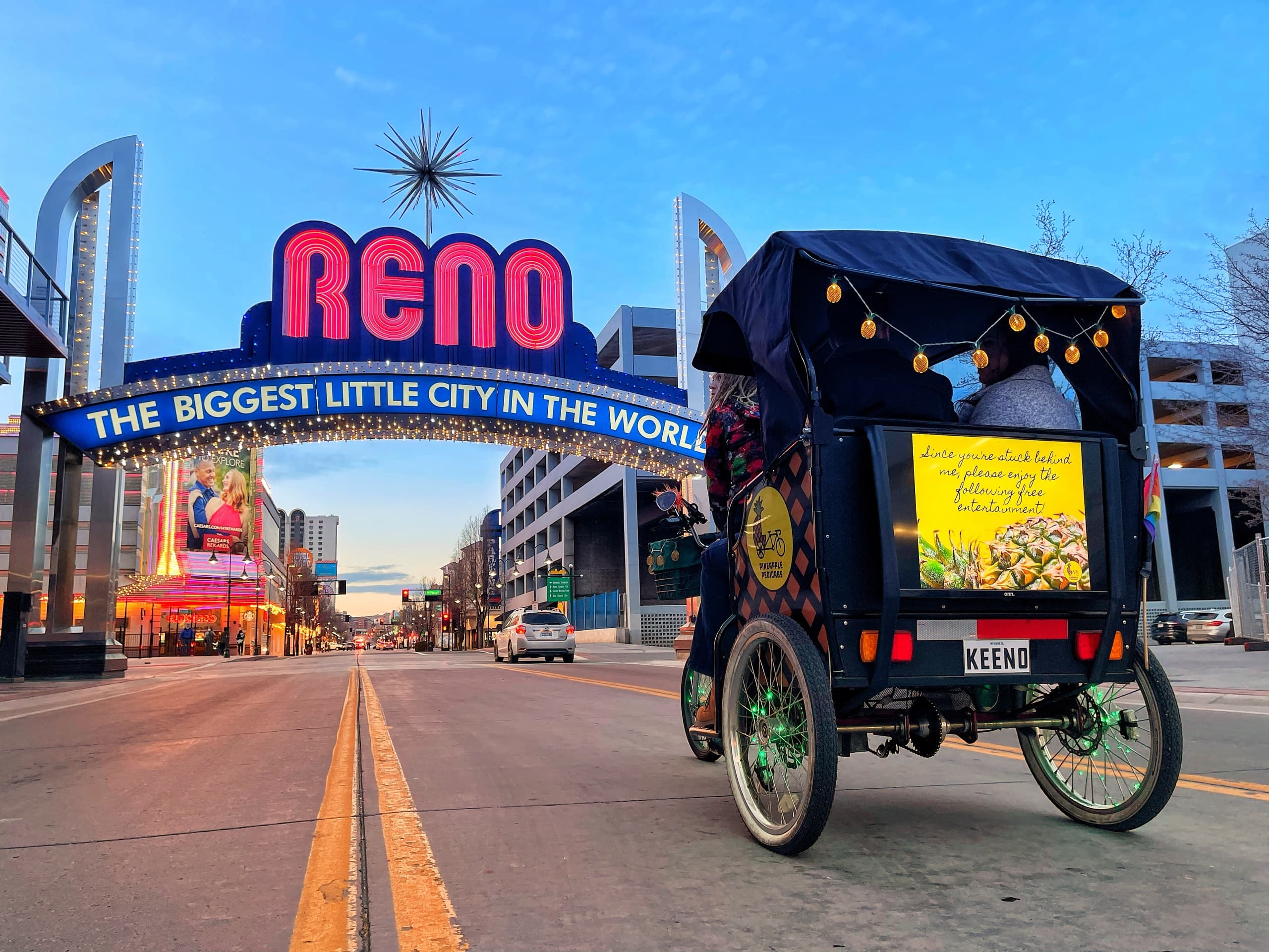 Pedicab parked under Reno arch on downtown street at dusk