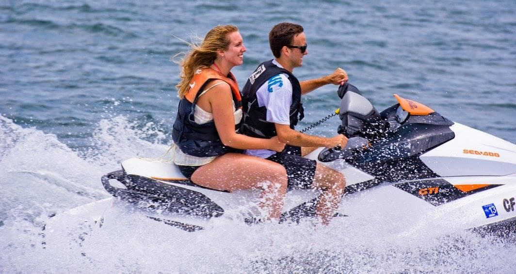 Two-person jetski speeding across ocean near coastal harbor