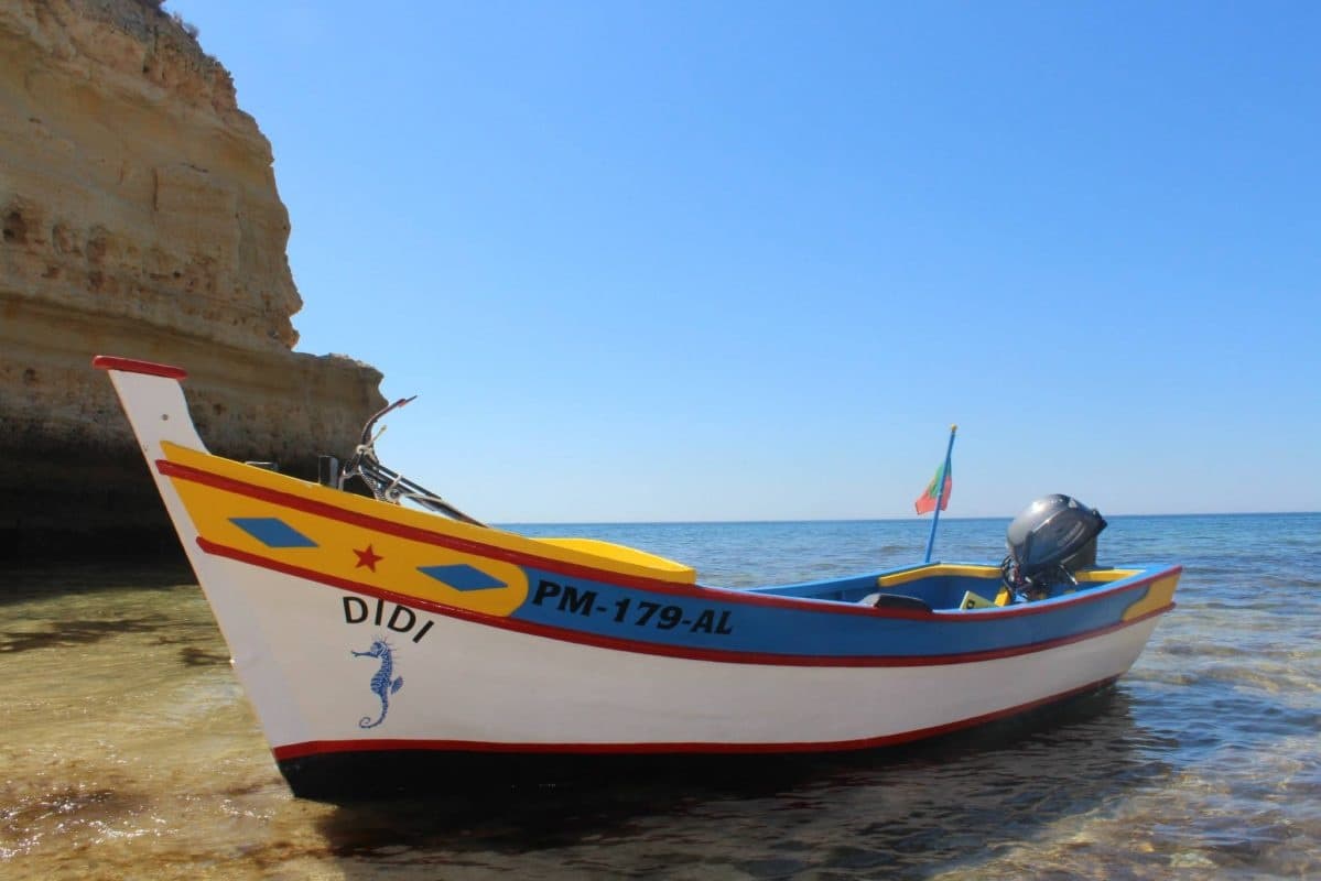 Traditional fishing boat beached by limestone cliffs on clear sea