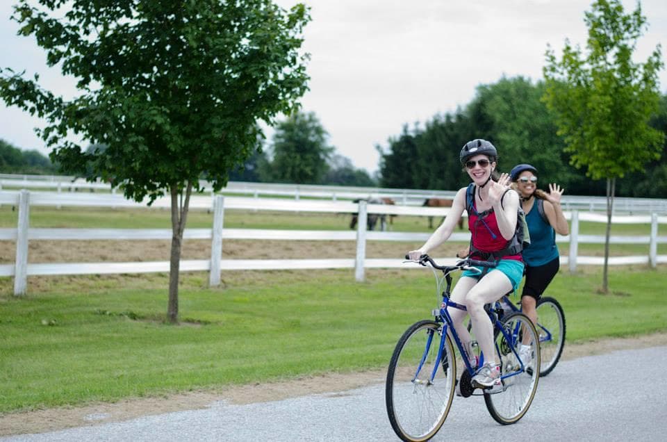 Cyclists riding scenic country road past white fence