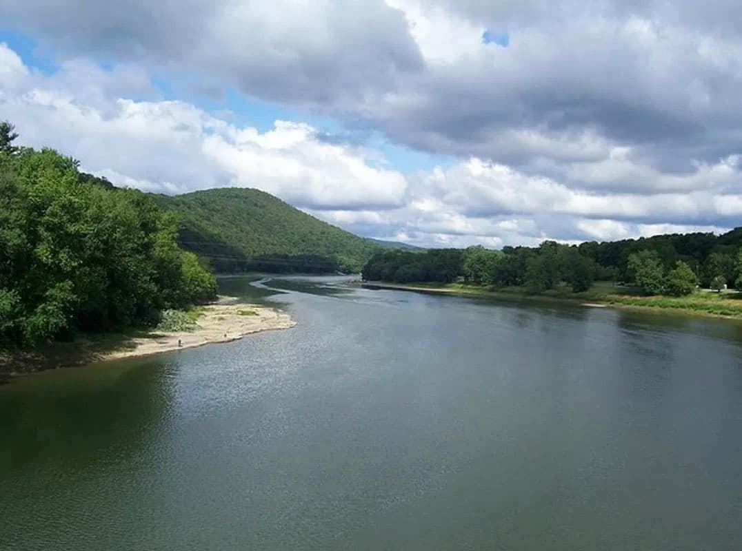 Wide river panorama with green hills and cloudy summer sky