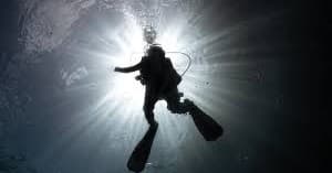 Silhouette scuba diver ascending toward sunlit surface underwater