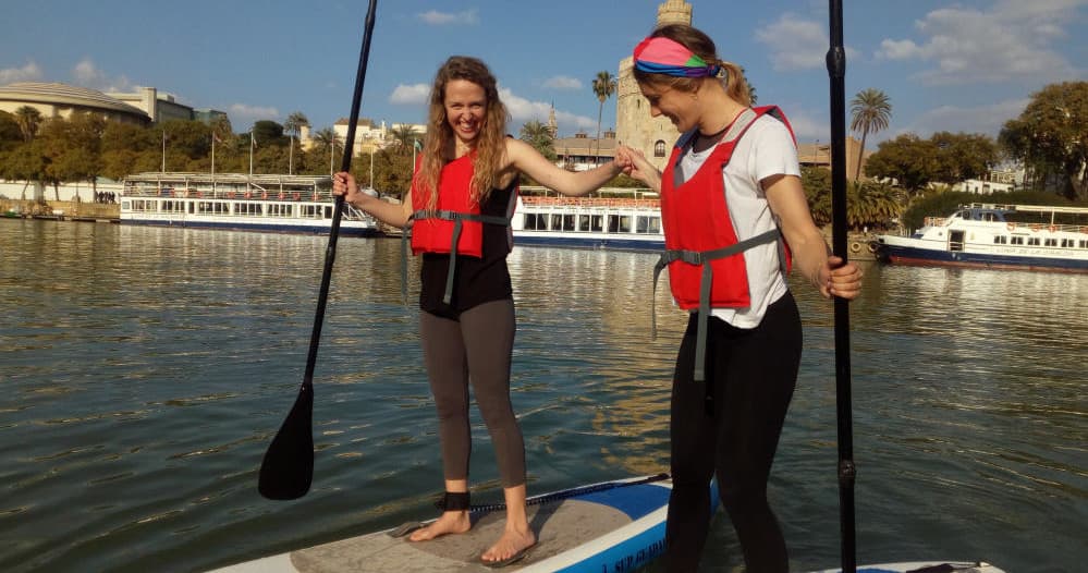 Two people learning stand-up paddleboarding on calm Guadalquivir