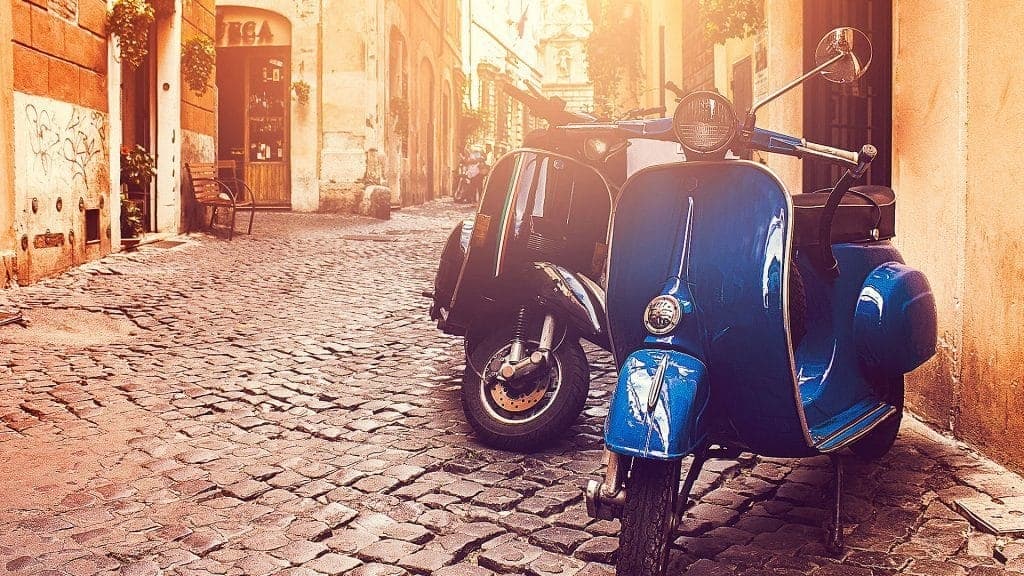 Vintage blue scooter parked on sunlit cobblestone alleyway