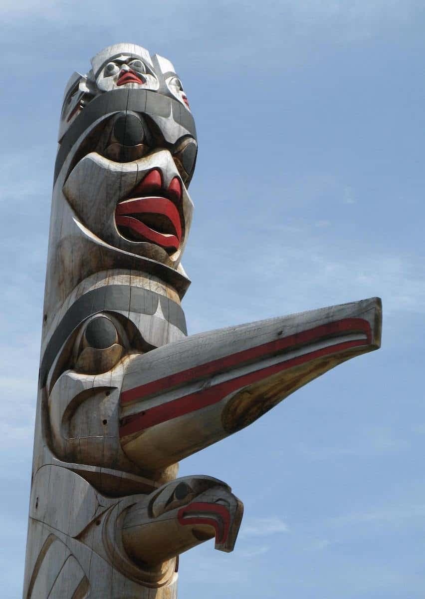 Carved totem pole art standing against blue sky on village grounds
