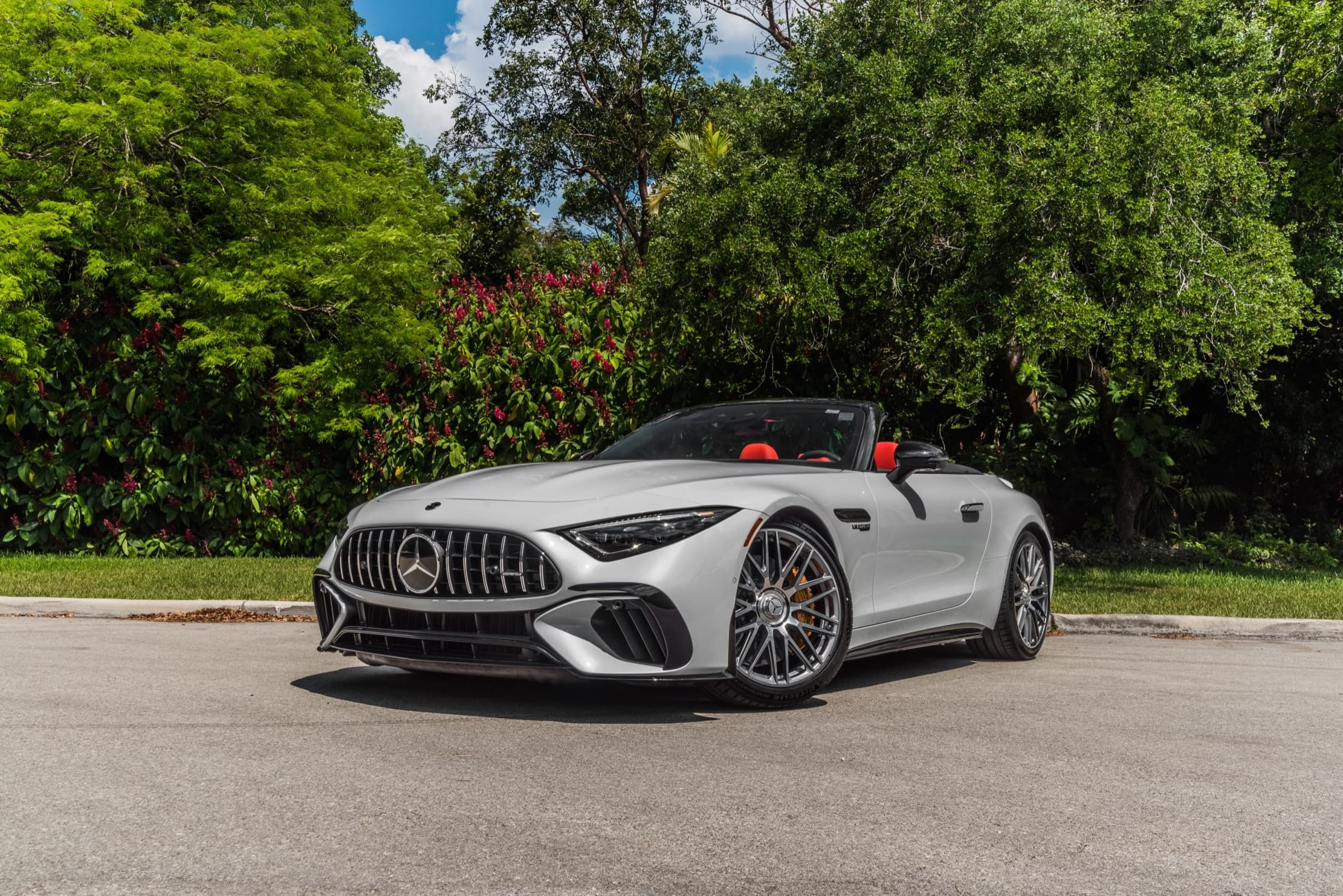 Silver Mercedes-AMG convertible cruising past lush tropical trees