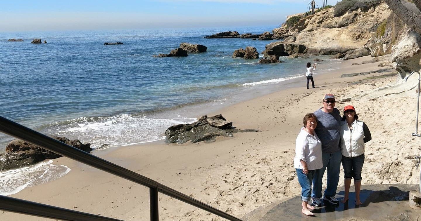Small group standing on sandy beach below ocean cliffs, California