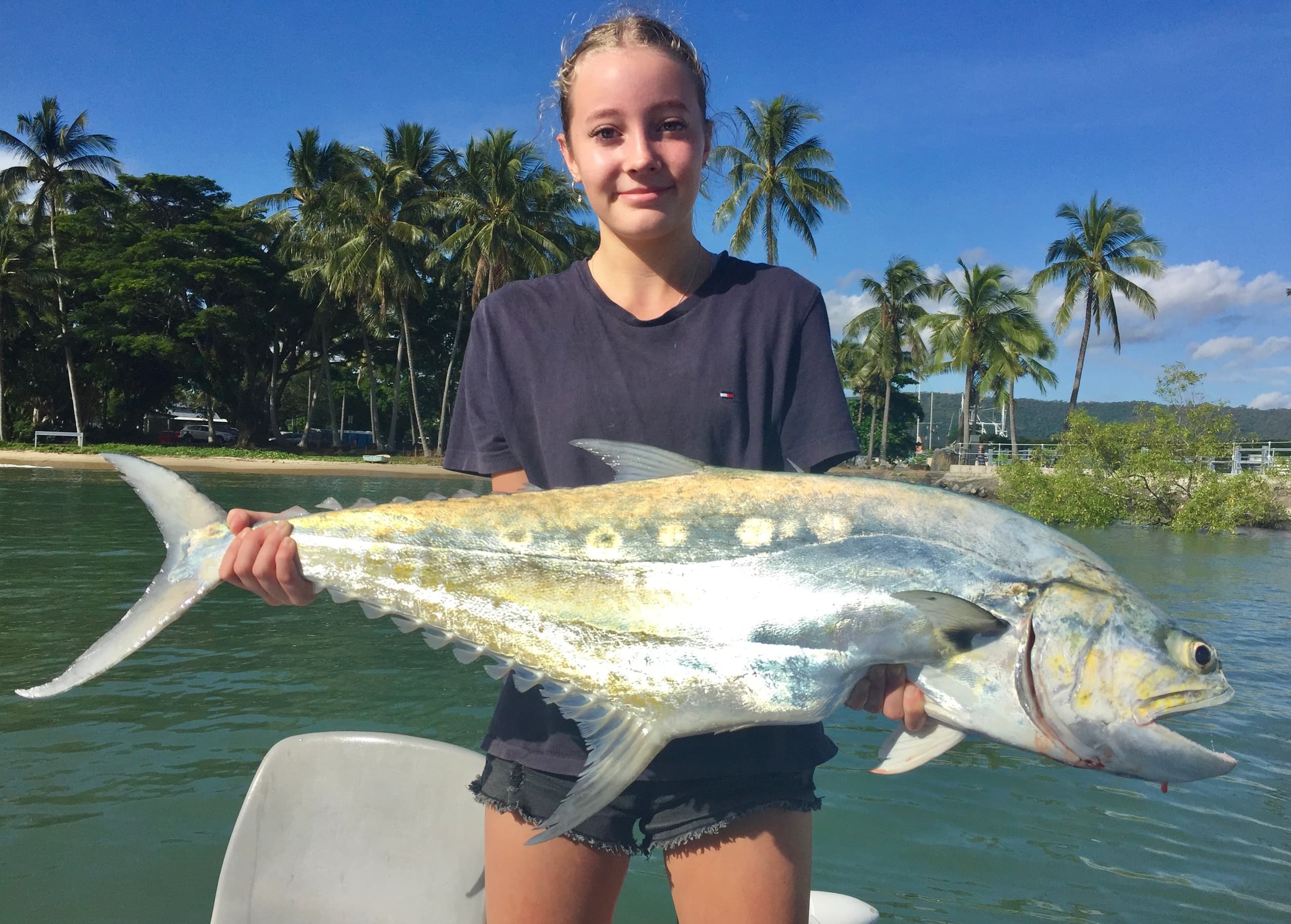 Young angler holding large kingfish near tropical shoreline