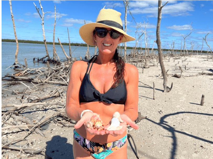 Woman on sandy mangrove beach holding seashells under blue sky