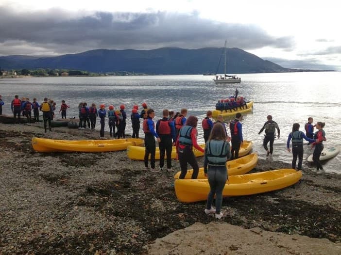Group preparing yellow sea kayaks on rocky shoreline at dawn