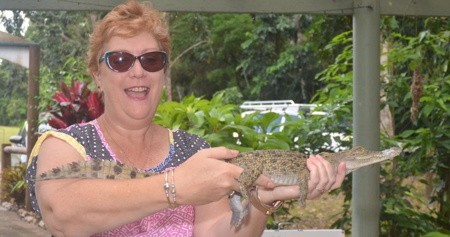 Tourist holding juvenile crocodile beside tropical river, close encounter