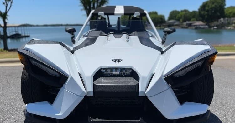 Three-wheeled roadster parked by lakeshore for scenic open-air drive