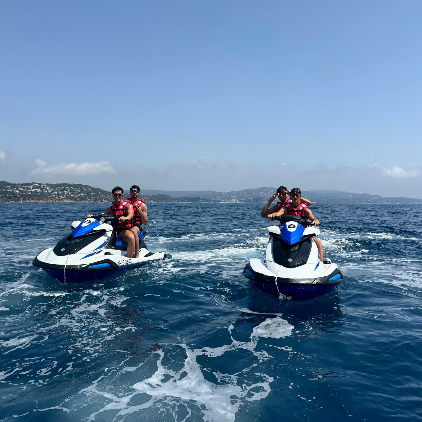 Two riders on jet skis cruising offshore with coastal backdrop