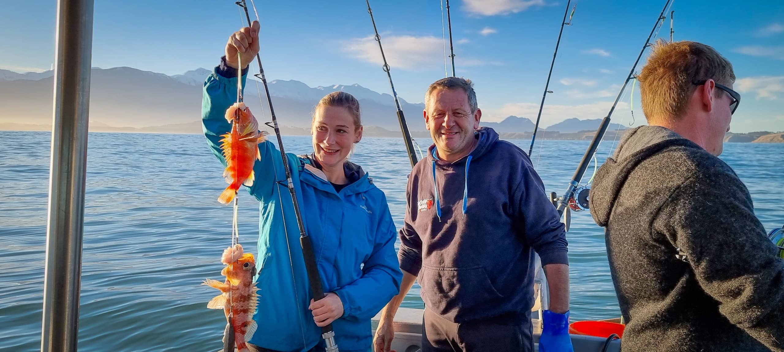Anglers on fishing charter holding catch against coastal mountains