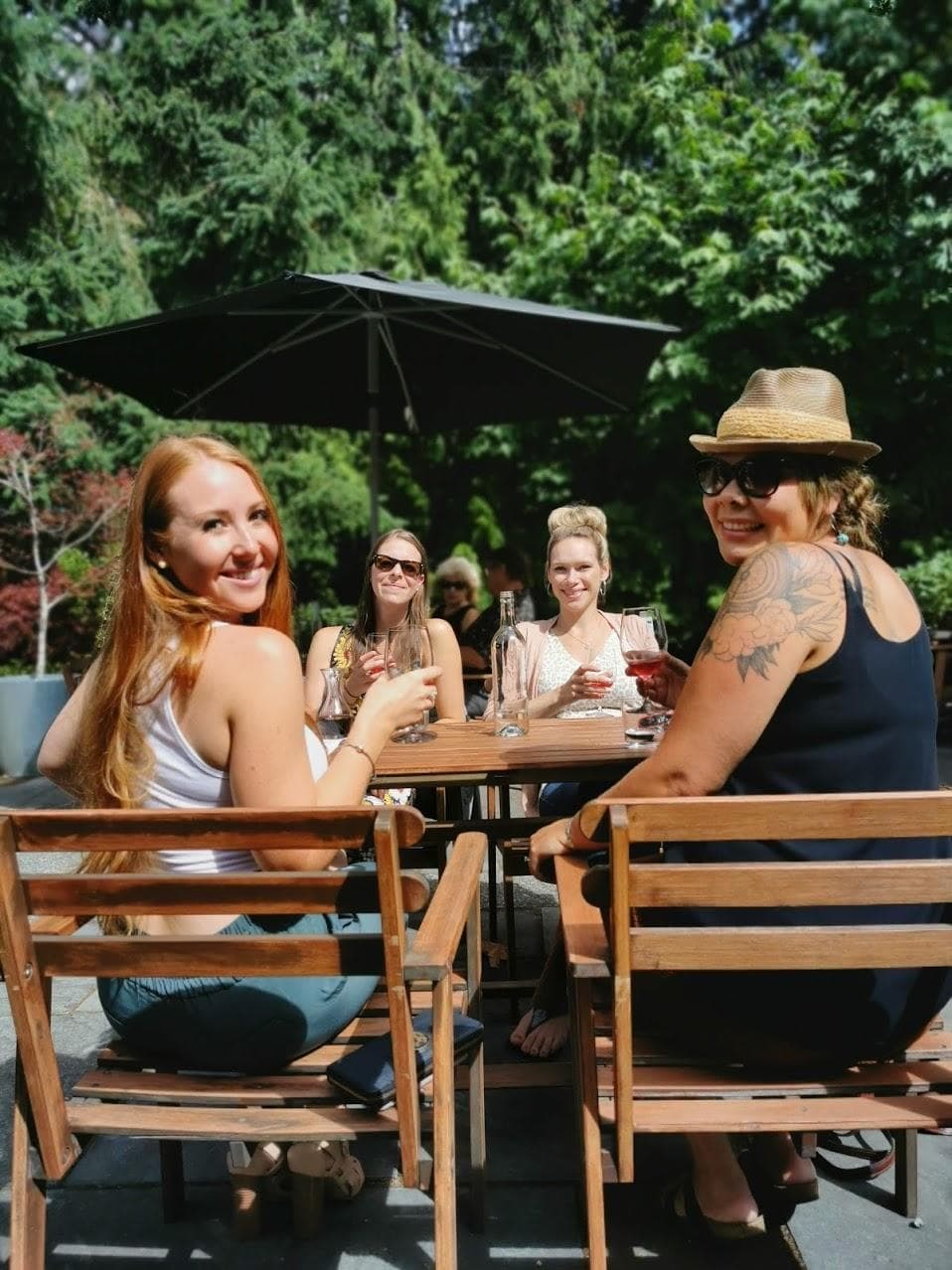 Friends seated at sunlit picnic table in leafy beer garden