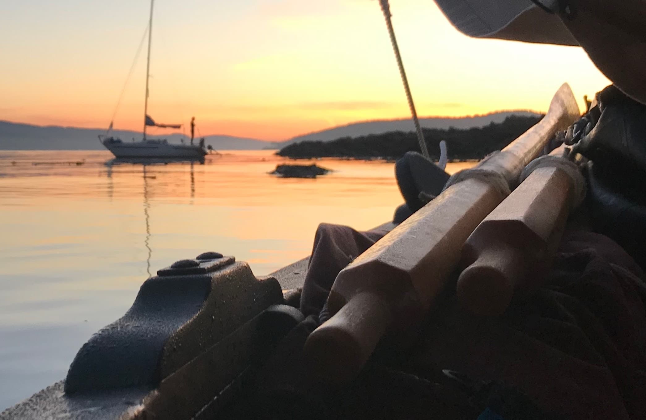 Rowboat oars and sunset with anchored sailboat on calm bay